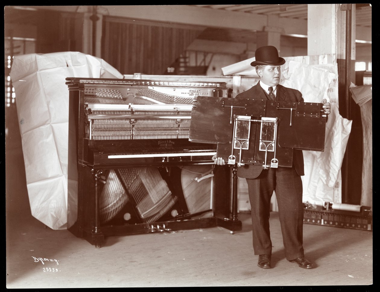 A Piano by Ricca und Son Piano Co. with a Man Adjacent Holding Up Part of the Piano Works by Byron Company