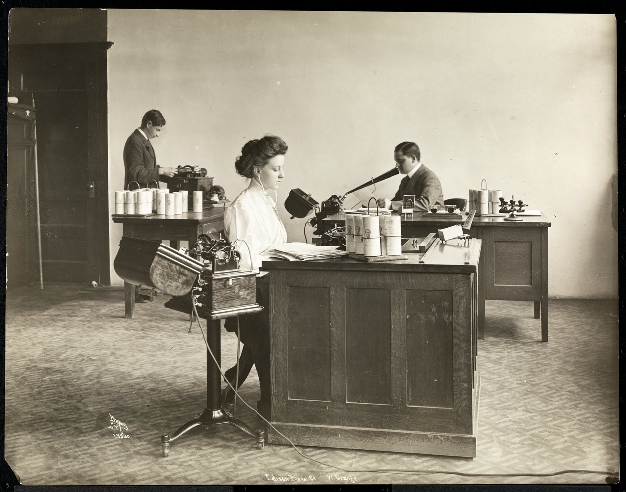 Interior view of a woman typing from a dictating machine and a man dictating into another at the Edison Phonograph Co., West Orange, New Jersey by Byron Company