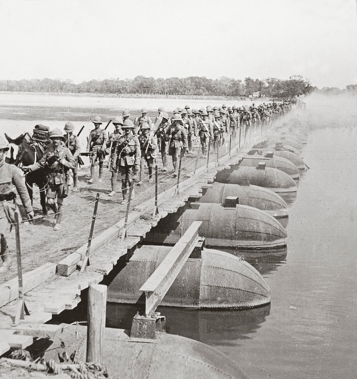 Machine gun section and infantry crossing a flooded river by pontoon bridge by English Photographer