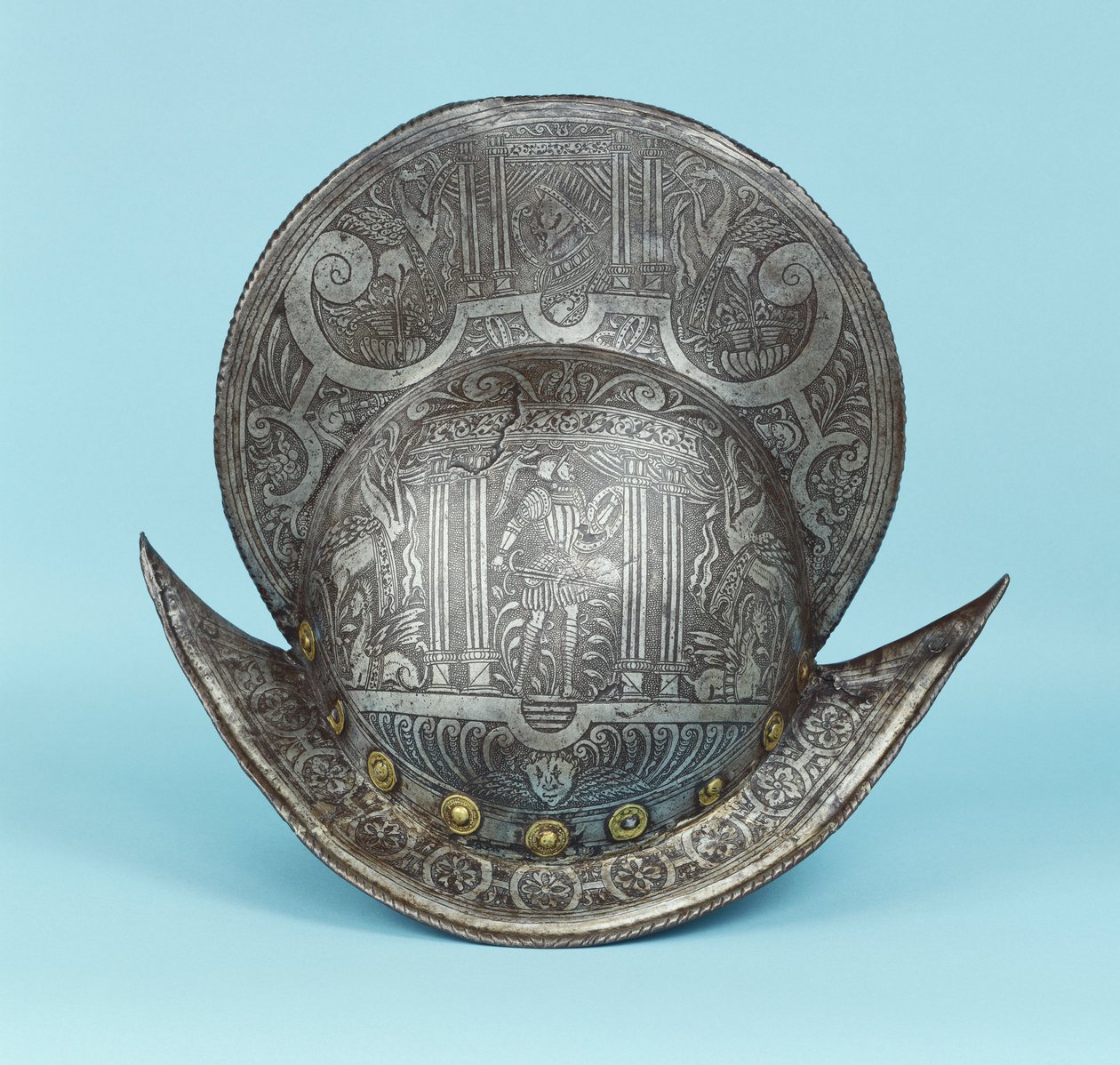 A comb morion, etched with cherub heads, sphinxes and winged horses, the centre with a pseudo classical warrior in contemporary armour with sword and shield by German School