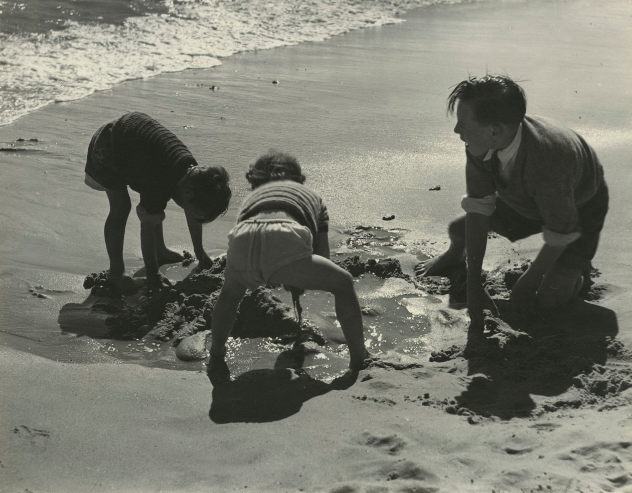 Three kids playing with sand at the beach by Godfrey Macdominic