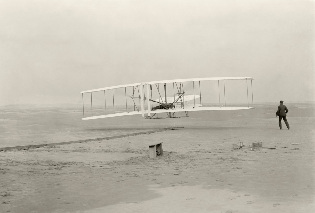 The Wright Flyer I makes its first flight of 120 feet in 12 seconds, at Kitty Hawk, North Carolina by John T. Daniels