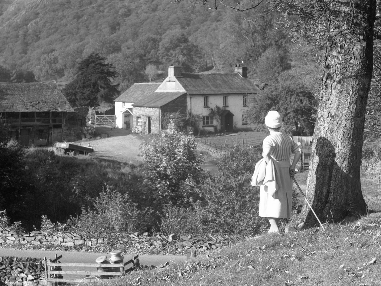 A woman stands next to a tree with her back to the camera looking out towards Yew Tree Farm by Joseph Hardman