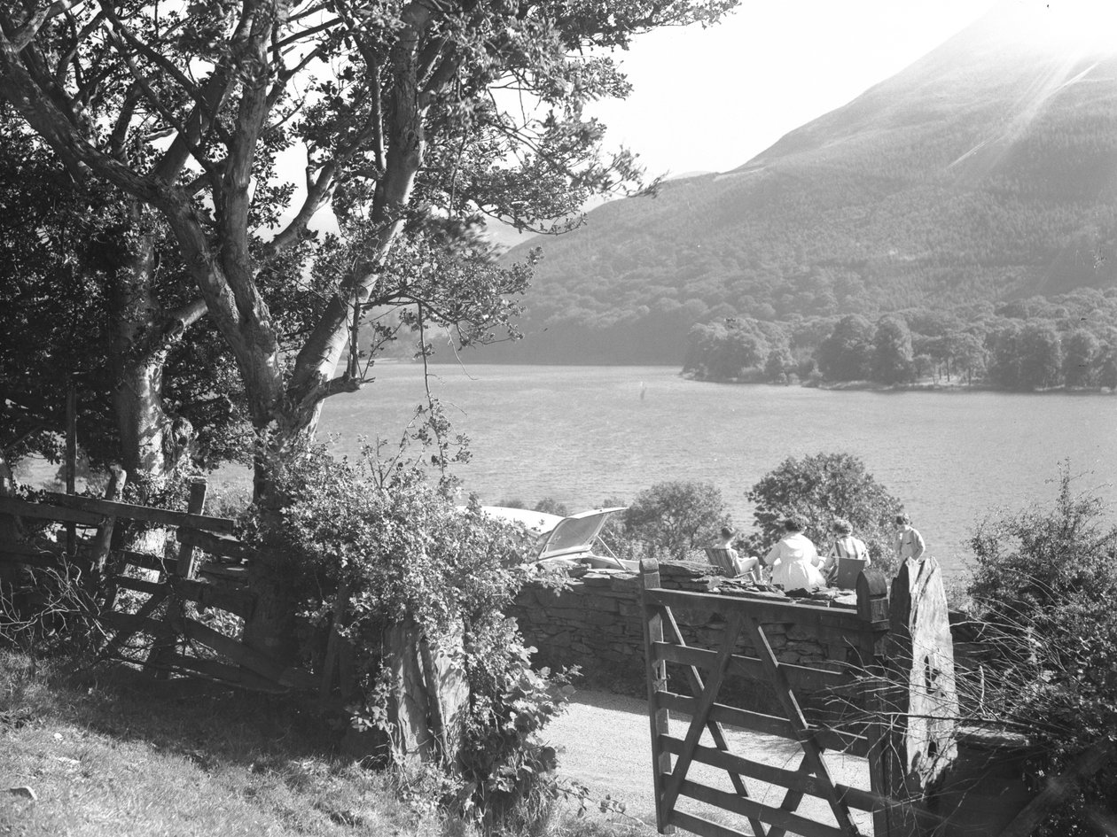 Four people having a picnic on a dry stone wall overlooking a lake, car parked with boot open by Joseph Hardman