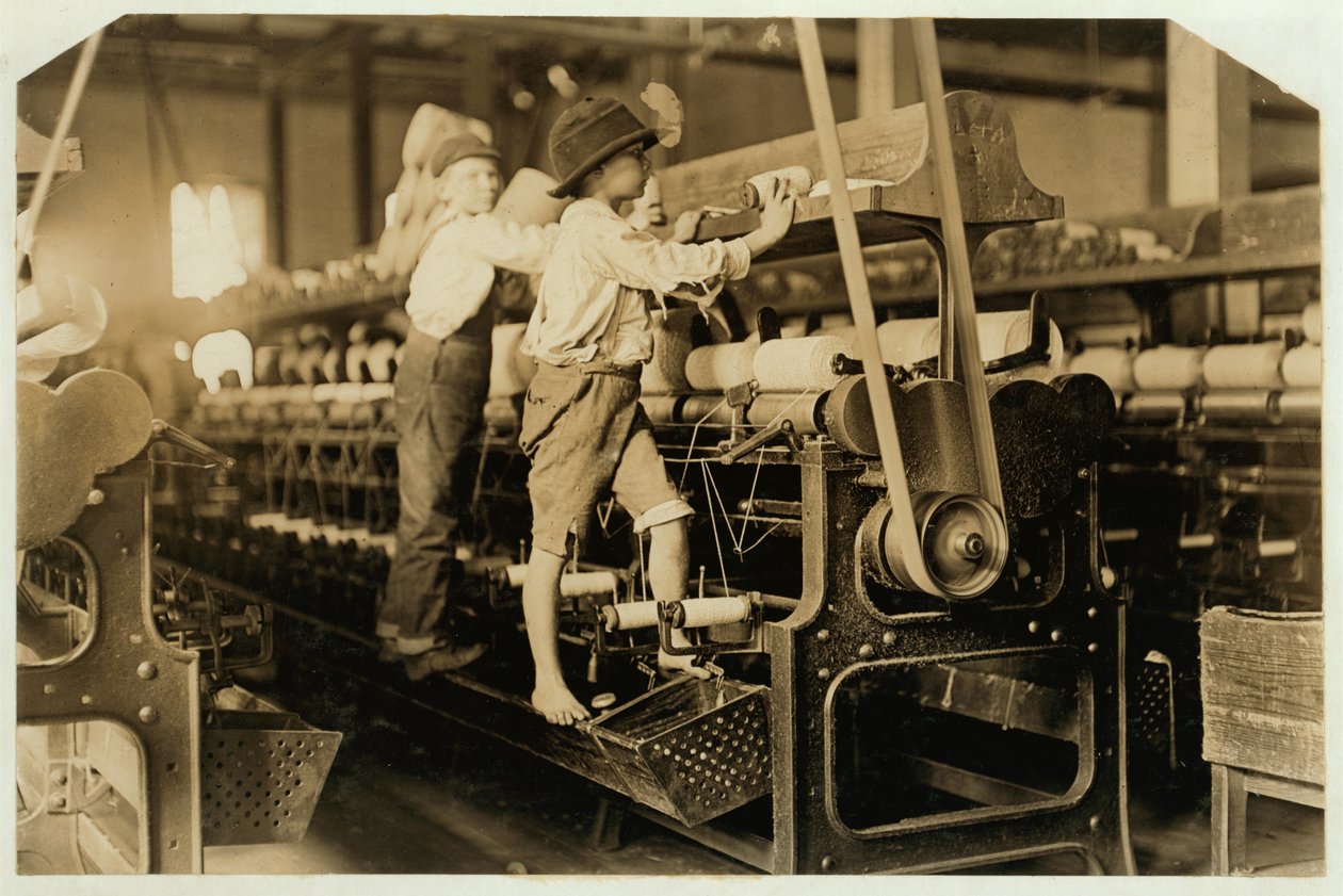 Small boys climbing on spinning frame to mend broken threads and replace empty bobbins at Bibb Mill, Macon, Georgia, 1909 by Lewis Wickes Hine