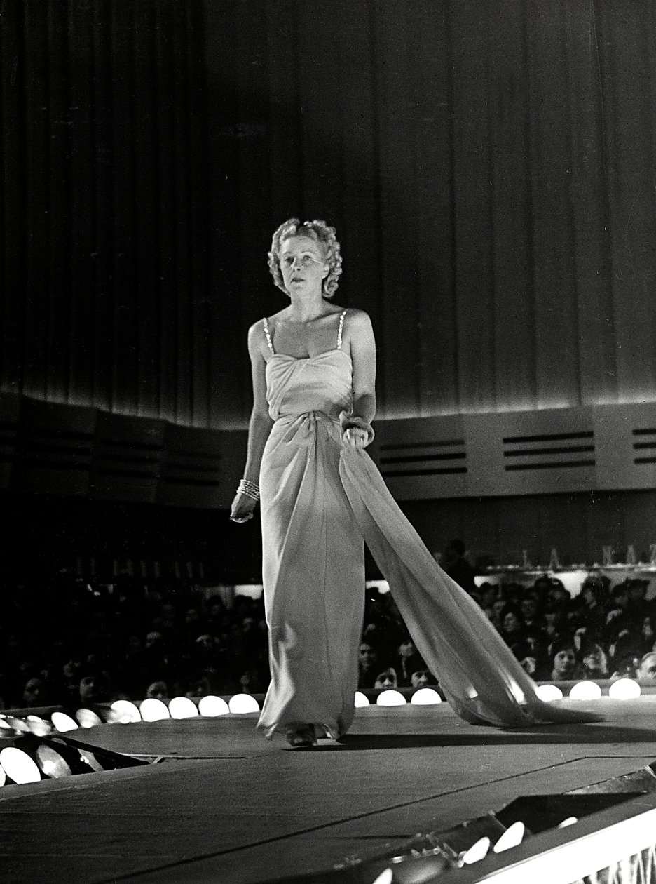 Model photographed on a runway in evening dress with rhinestone shoulder straps; the article is a creation of the couture house 