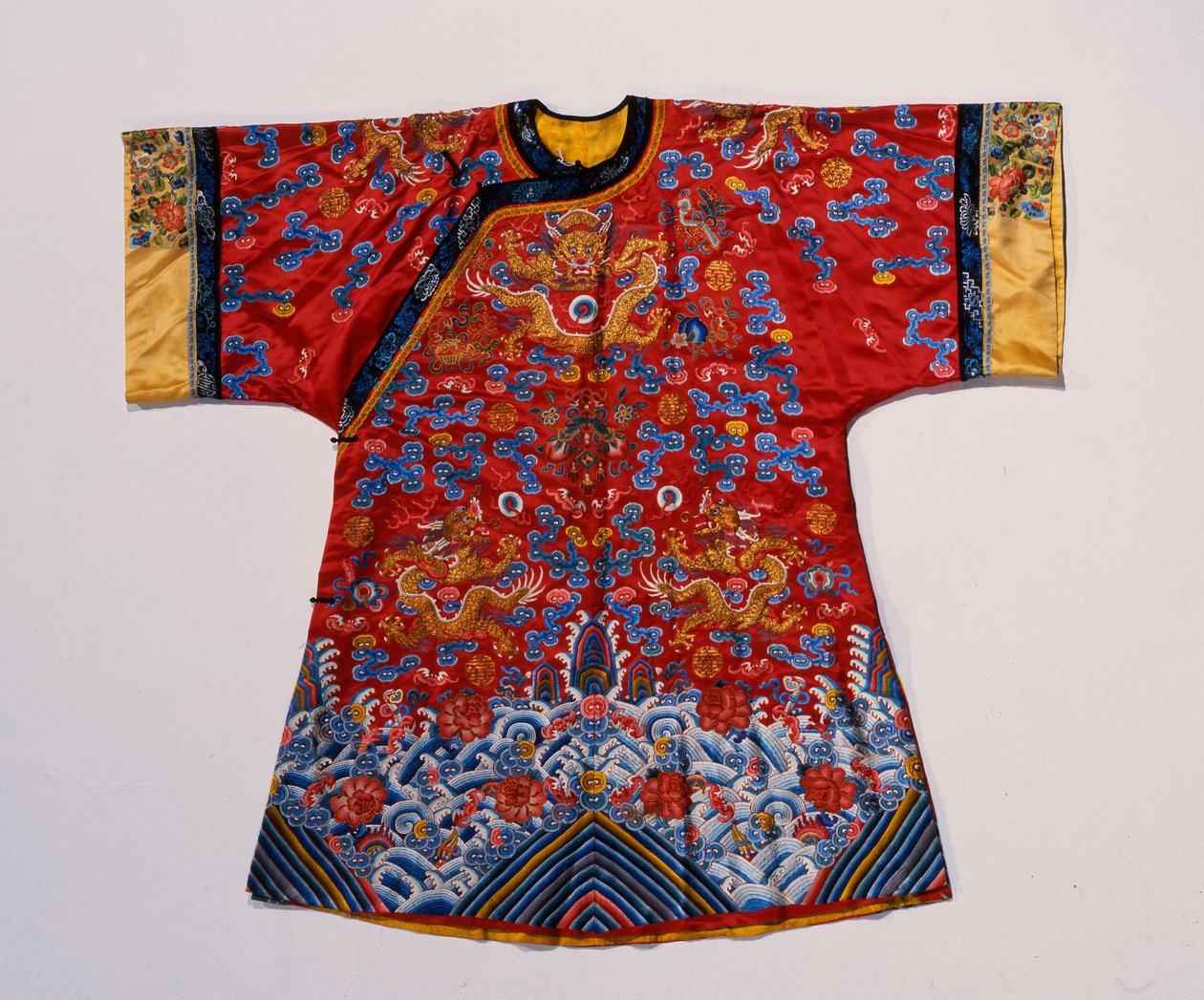 A semi formal robe of red satin embroidered in silks and gilt thread with dragons amidst scrolling clouds above a turbulent sea wave border by School Chinese