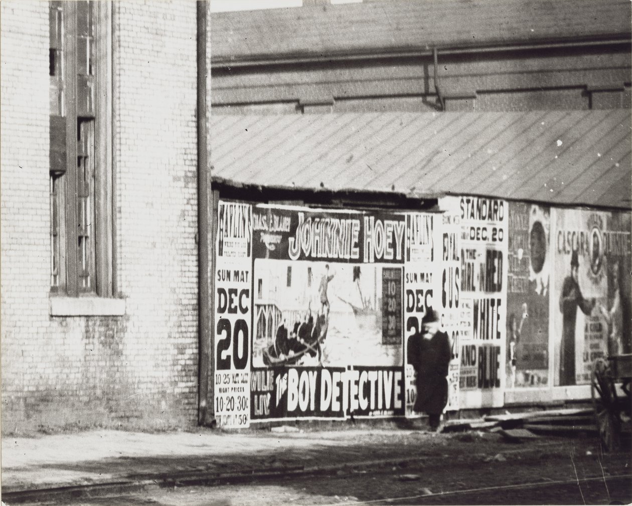 A man walks past a wall of poster advertisements including one for Johnnie Hoey The Boy Detective playing at Havlin