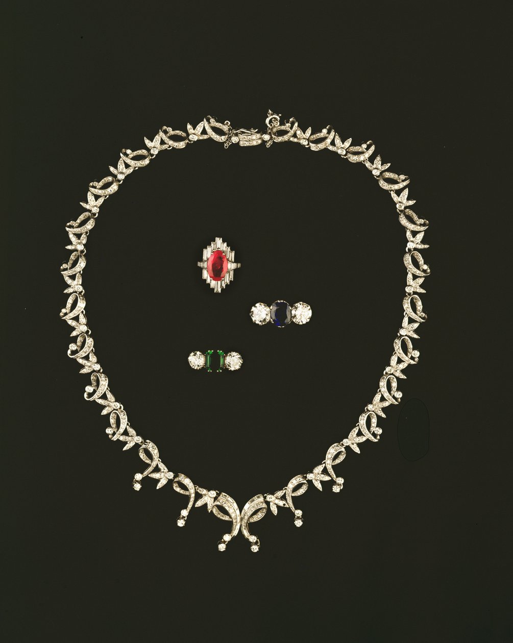 Art Deco scroll and leaf design necklace; ruby and diamond baguette cluster ring; sapphire and diamond three stone ring; emerald and diamond three stone ring by Unbekannt Unbekannt