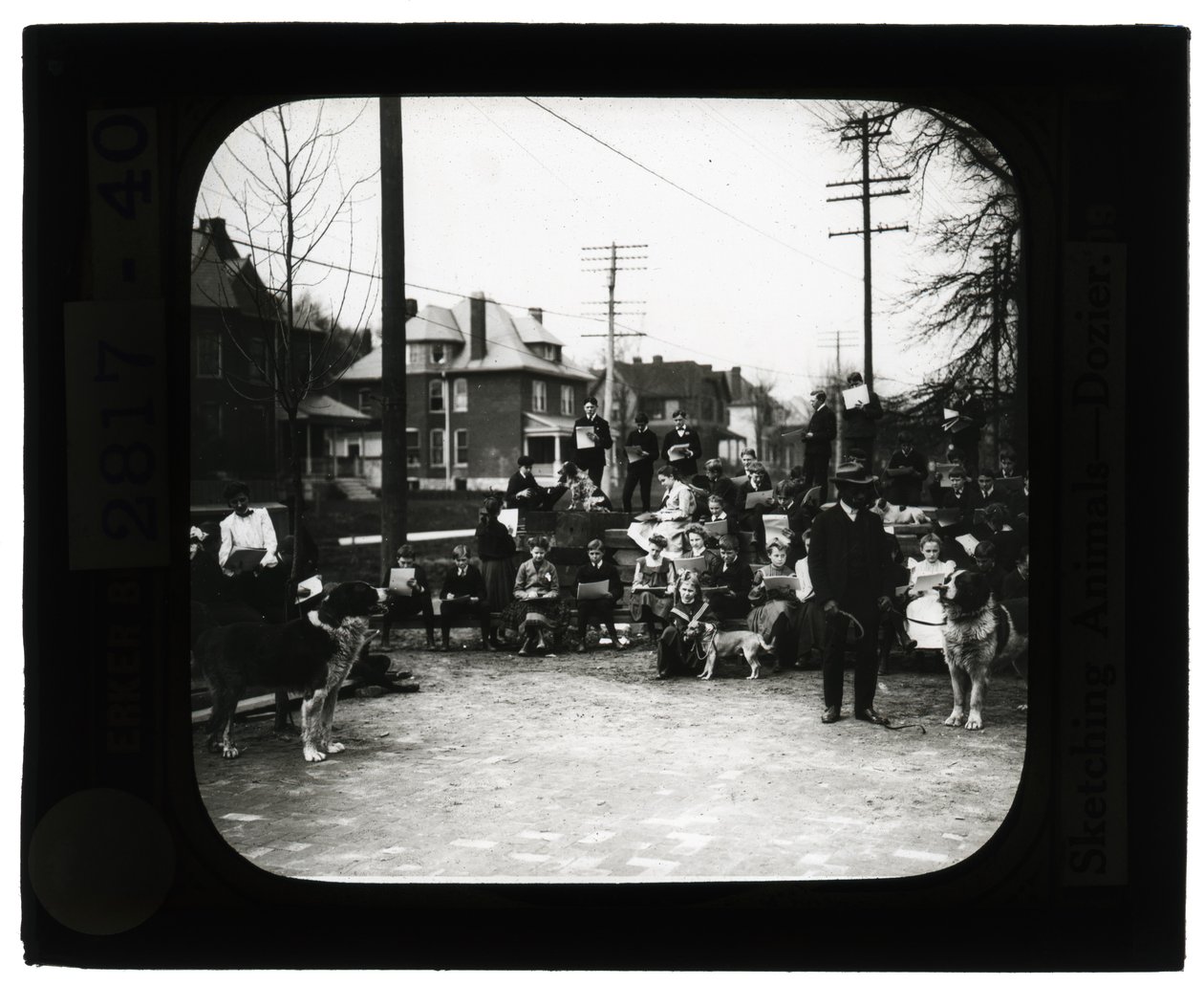 Horizontal, black and white photo of students drawing dogs in an outdoor classroom setting by Unknown