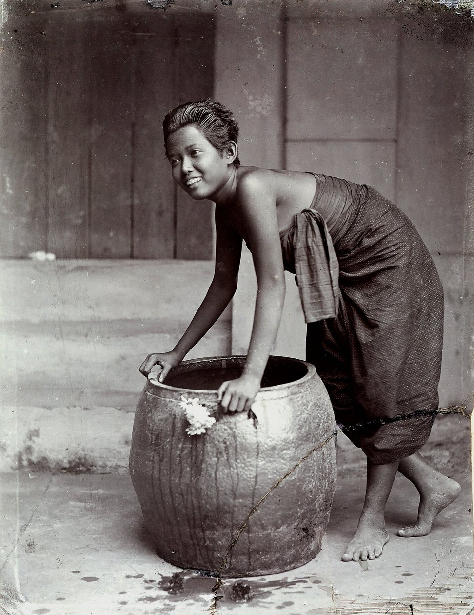 Young smiling Thai woman, pushing a large container by Unknown photographer