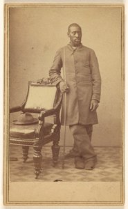 Black Soldier Standing Near Chair with Hat in Seat
