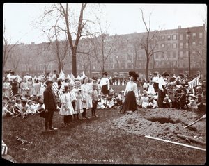 Adults and children holding flags standing around a newly dug hole for a tree planting on Arbor Day at Tompkins Square Park, New York