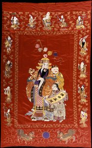 A Chinese Embroidered Red Satin Hanging Depicting a Figure with a Ru-i and Two Attendants, the Borders Decorated with the Eight Immortals