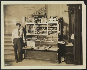 Blind news dealer, John Martie, at his stand at the south end of the Municipal Building, New York by Company Byron
