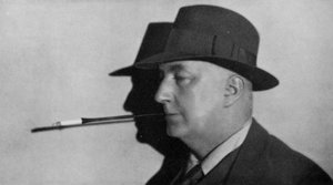 Portrait of Edgar Wallace, wearing hat and smoking cigarette in holder
