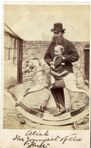 Young girl on a rocking horse in the garden, her father beside