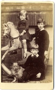 Young girl on rocking horse with one boy standing and one boy seated with dog