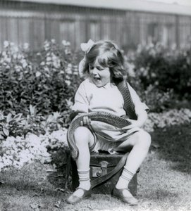A young girl Betty holding an Eastern Indigo Snake, while sitting on a leather trunk, London Zoo, 1924