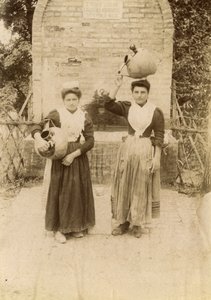 Two young women wearing traditional clothes and carrying terracotta jars near well, Marche, Italy, circa 1910 by Italian Photographer