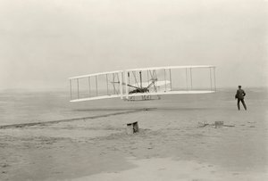 The Wright Flyer I makes its first flight of 120 feet in 12 seconds, at Kitty Hawk, North Carolina by John T. Daniels