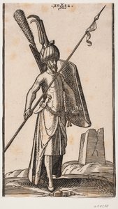 Standing soldier with curved shield in left hand and spear in right hand; sword at his left side, a dagger stuck in the belt at his left side; in the background to the right, the ruin of an obelisk or a tower with a square base