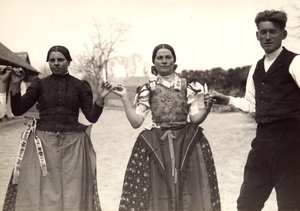 Two ladies and a man, in Hungarian traditional dresses, are holding hands in a dance, holding some candles in their hands