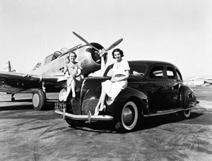California: 1939 Two women sit on the fenders of a 1939 Lincoln Zephyr sedan at an airport with a single engine plane parked behind them by Unbekannt
