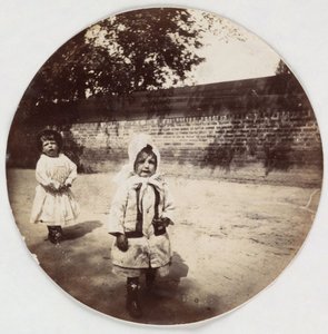 Two small children walking alongside a wall, c 1890