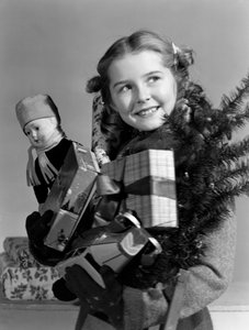 Young girl carrying an armful of Christmas presents, c 1950