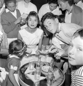 The Actress and Fashion Model Elsa Martinelli at the XVIII International Film Festival in Venice Lido (She Signs Autographs with Young Fans. On the Table, a Bottle of Schweppes) - 1957