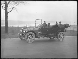 Three unidentified people and two Chow dogs driving in a convertible car along a river or lake