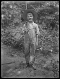 William Gray Hassler in straw hat and overalls, carrying fishing pole and basket in the woods