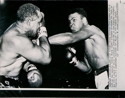 Young Cassius Clay scores with a left against the veteran Archie Moore in the first round of the fight in Los Angeles by American Photographer