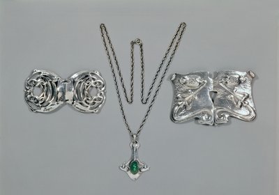 Silver jewellery designed for Liberty. Left to right: Waist clasp with interlaced Celtic design, 1904. Pendant and chain set with cabochon-cut chrysoprase. Waist clasp with repousse design on hammered by Archibald Knox