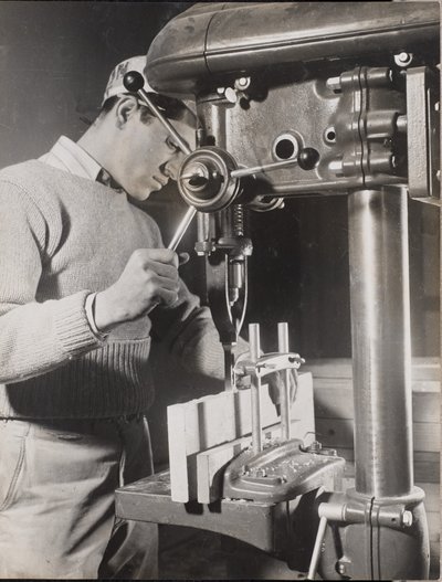 Man uses a machine to drill holes in two wood blocks by Arnold Eagle