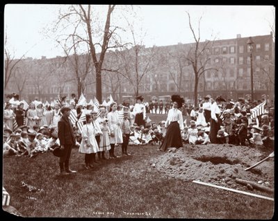 Adults and children holding flags standing around a newly dug hole for a tree planting on Arbor Day at Tompkins Square Park, New York by Byron Company
