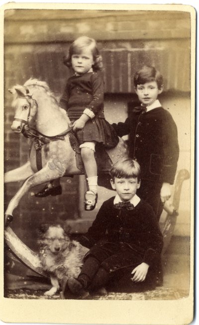 Young girl on rocking horse with one boy standing and one boy seated with dog by English School