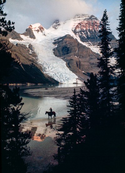 Lone horse and rider reflect on lake at base of Canada