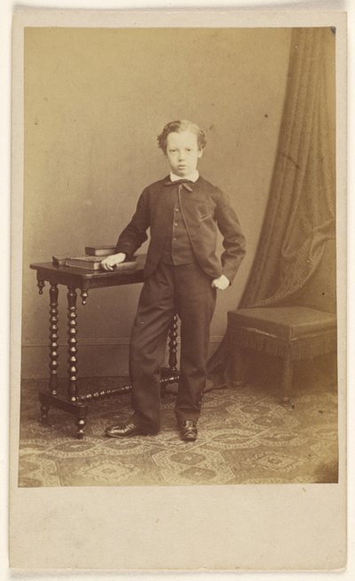 Unidentified little boy in suit standing at a table with books on top by Joseph Brown