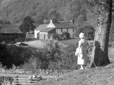A woman stands next to a tree with her back to the camera looking out towards Yew Tree Farm by Joseph Hardman
