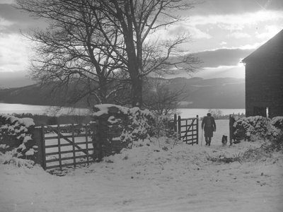 Man and dog walking through gate towards camera in snow with Thirlmere behind by Joseph Hardman