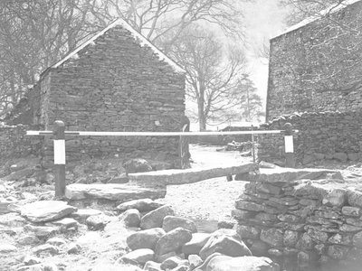 Stone slab bridge and handrail crossing stream with farm buildings behind by Joseph Hardman