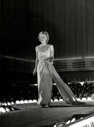Model photographed on a runway in evening dress with rhinestone shoulder straps; the article is a creation of the couture house 