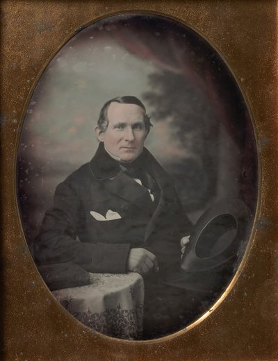 Man Wearing Coat and Gloves, Holding Hat, Seated in Front of Painted Outdoor Backdrop, 1840s by Samuel Broadbent Jr..