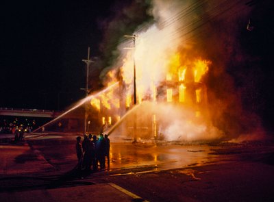 An urban building engulfed in fire and flames at night in Kansas City with firemen by Ted Spiegel