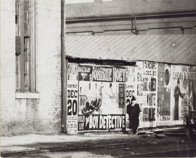 A man walks past a wall of poster advertisements including one for Johnnie Hoey The Boy Detective playing at Havlin