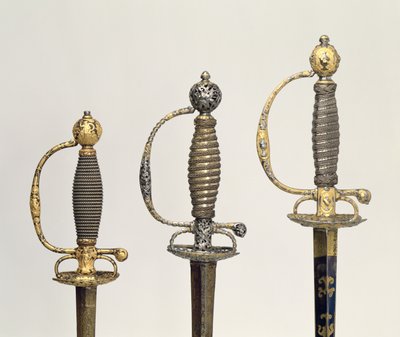 Hilts of three French swords: one of steel, blued and overlaid with designs in chased gold, c.1730; one of steel pierced and chiselled and the ground of matted gold, c.1760; one of chiselled steel by Unbekannt Unbekannt