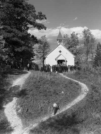 Men gathered outside of a small rural building, a schoolhouse or a church with bell by Volkmar Wentzel
