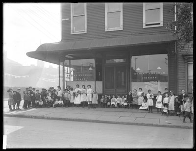 Children pose in front of an unidentified storefront branch of the Queens Borough Public Library, New York, c.1910 by William Davis Hassler